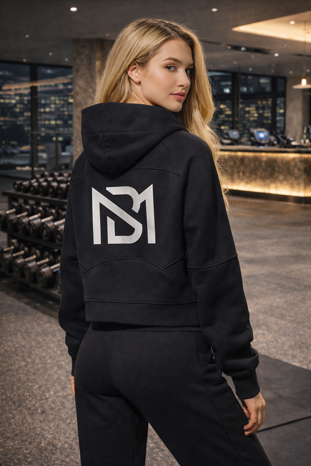Woman wearing a black hoodie with a logo in a gym setting